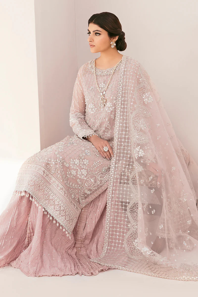 Woman in a traditional pink embroidered outfit with a matching dupatta on a plain background