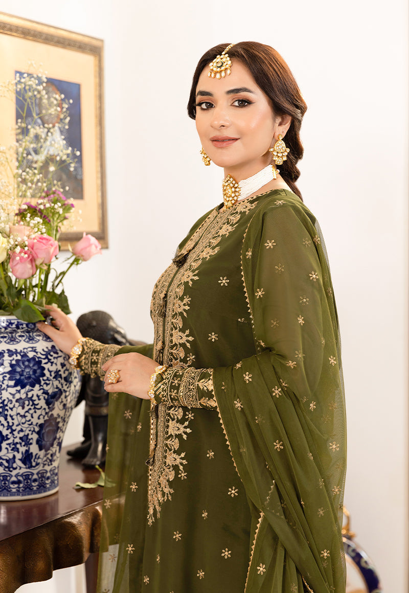 Woman in a green embroidered outfit with gold details, standing indoors.