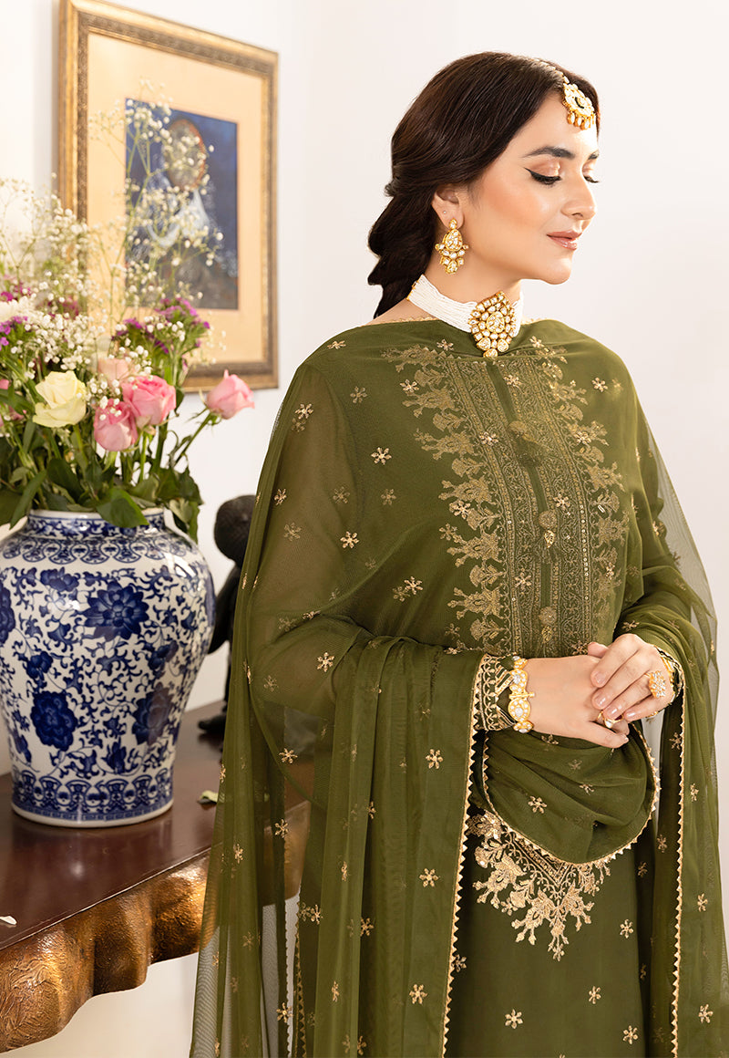 Woman in a green embroidered outfit standing next to a vase with flowers and a framed picture.