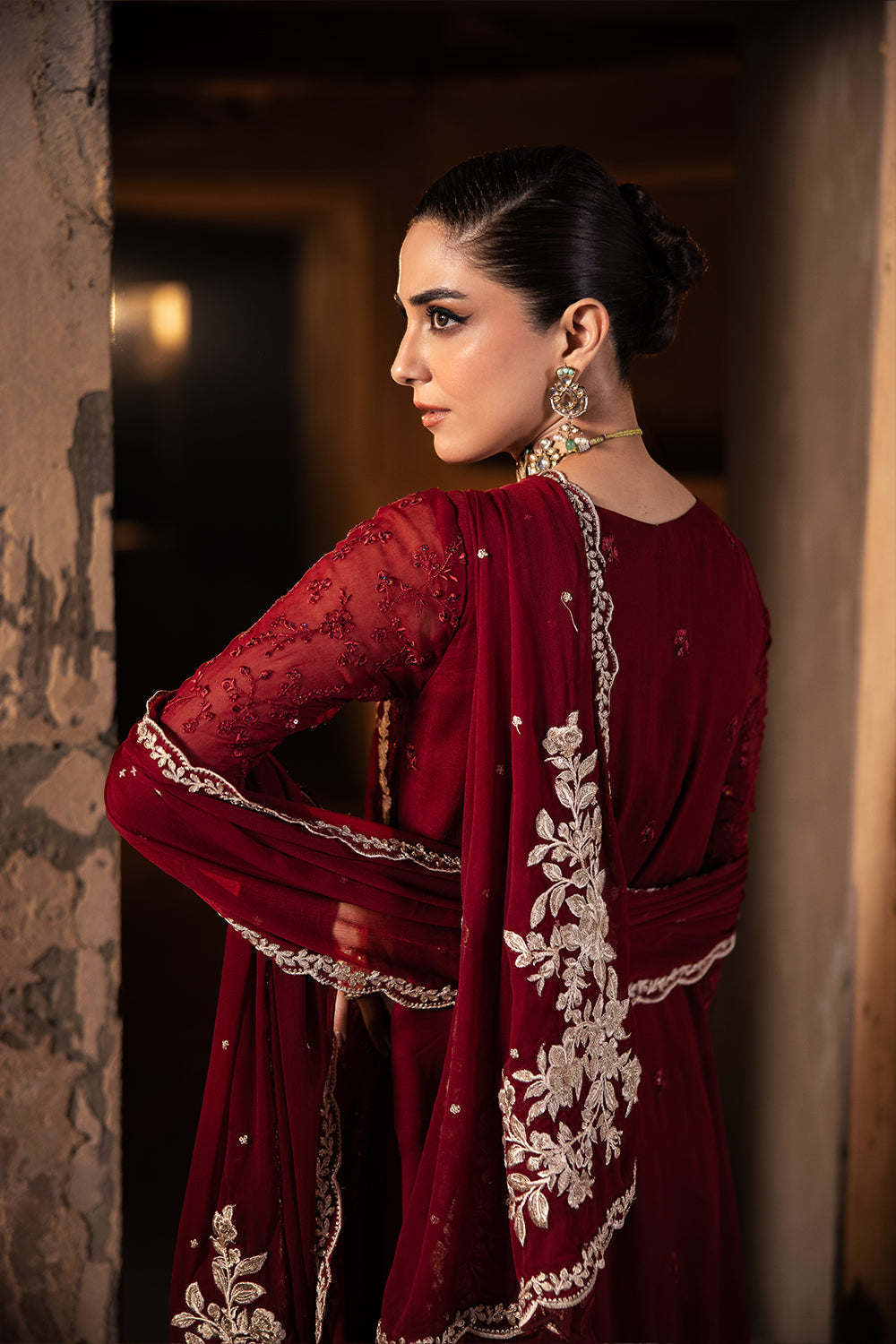 Woman in a red traditional outfit with white embroidery, standing indoors.