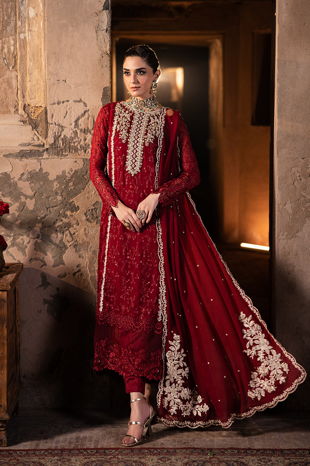 Woman in a red traditional outfit with white embroidery standing in a dimly lit room.
