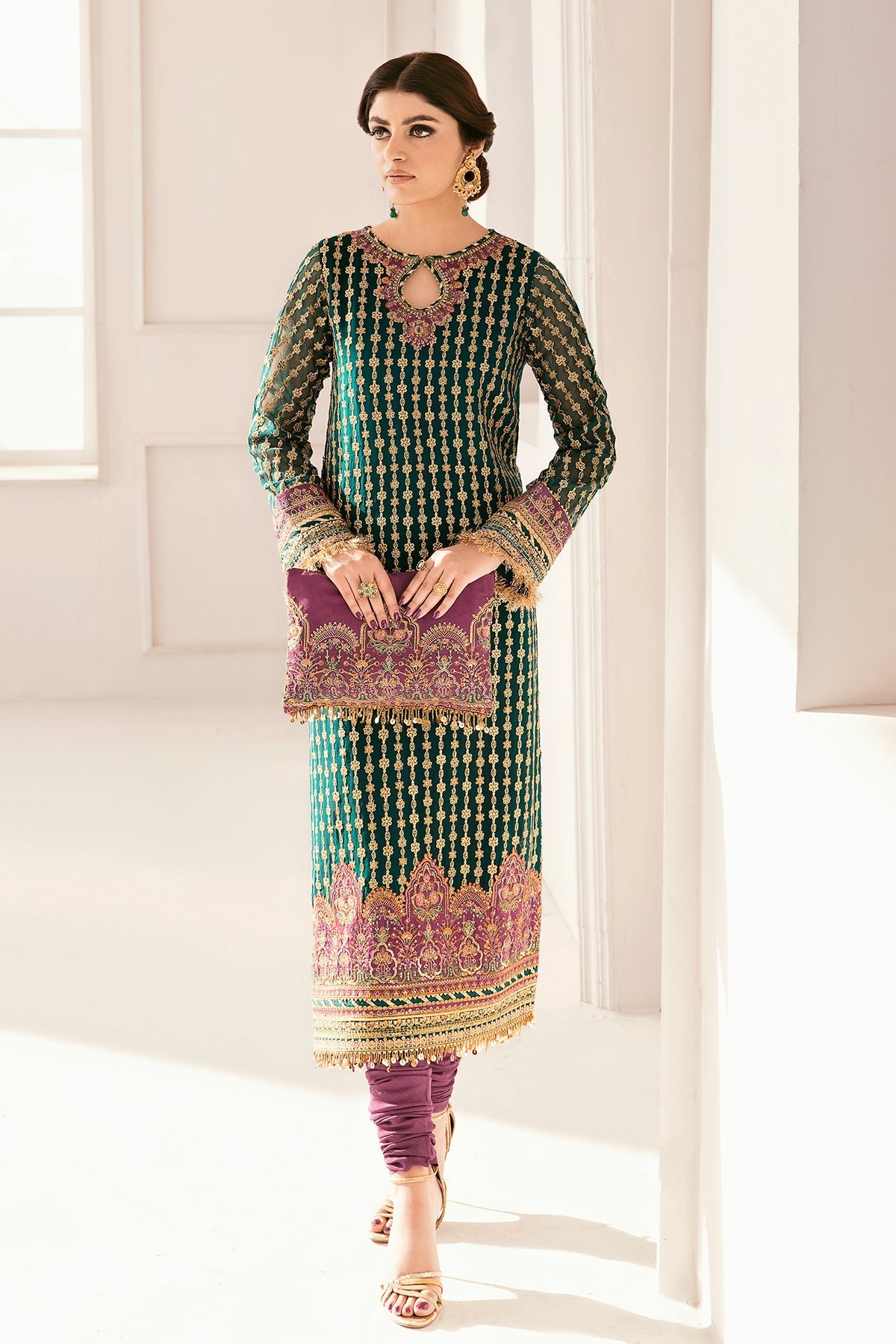 Woman wearing a traditional outfit with intricate patterns in a bright room.