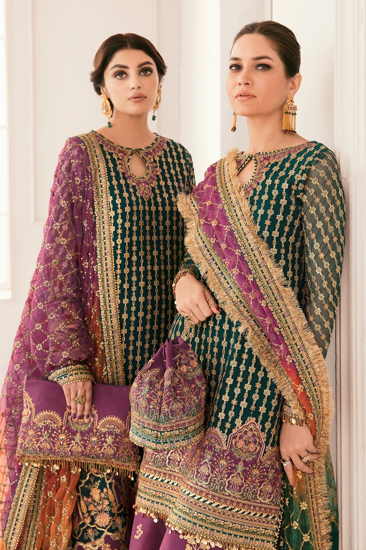 Two women in traditional embroidered outfits with a white curtain background
