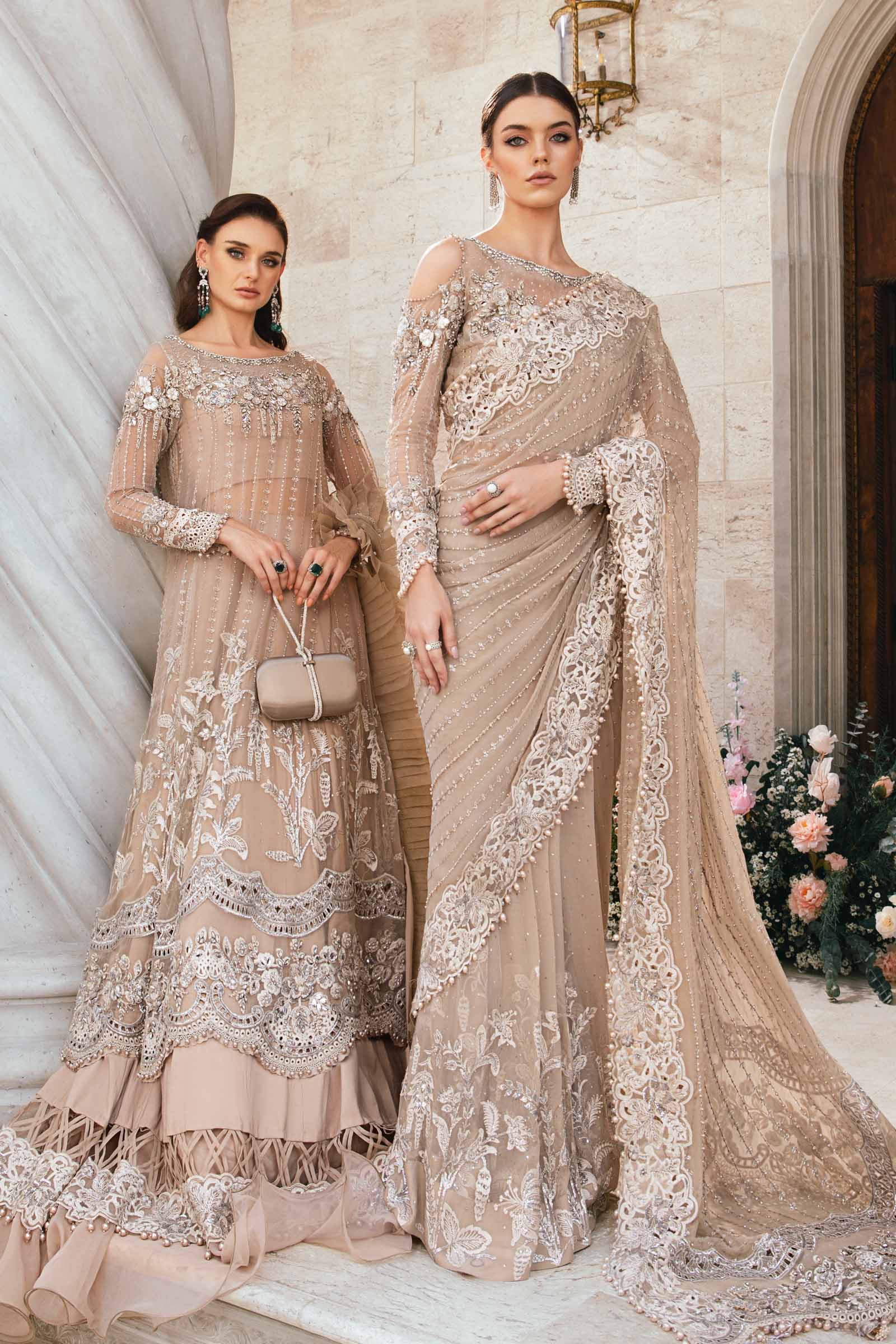 Two women in elegant beige and white embroidered dresses standing in a decorative interior setting.