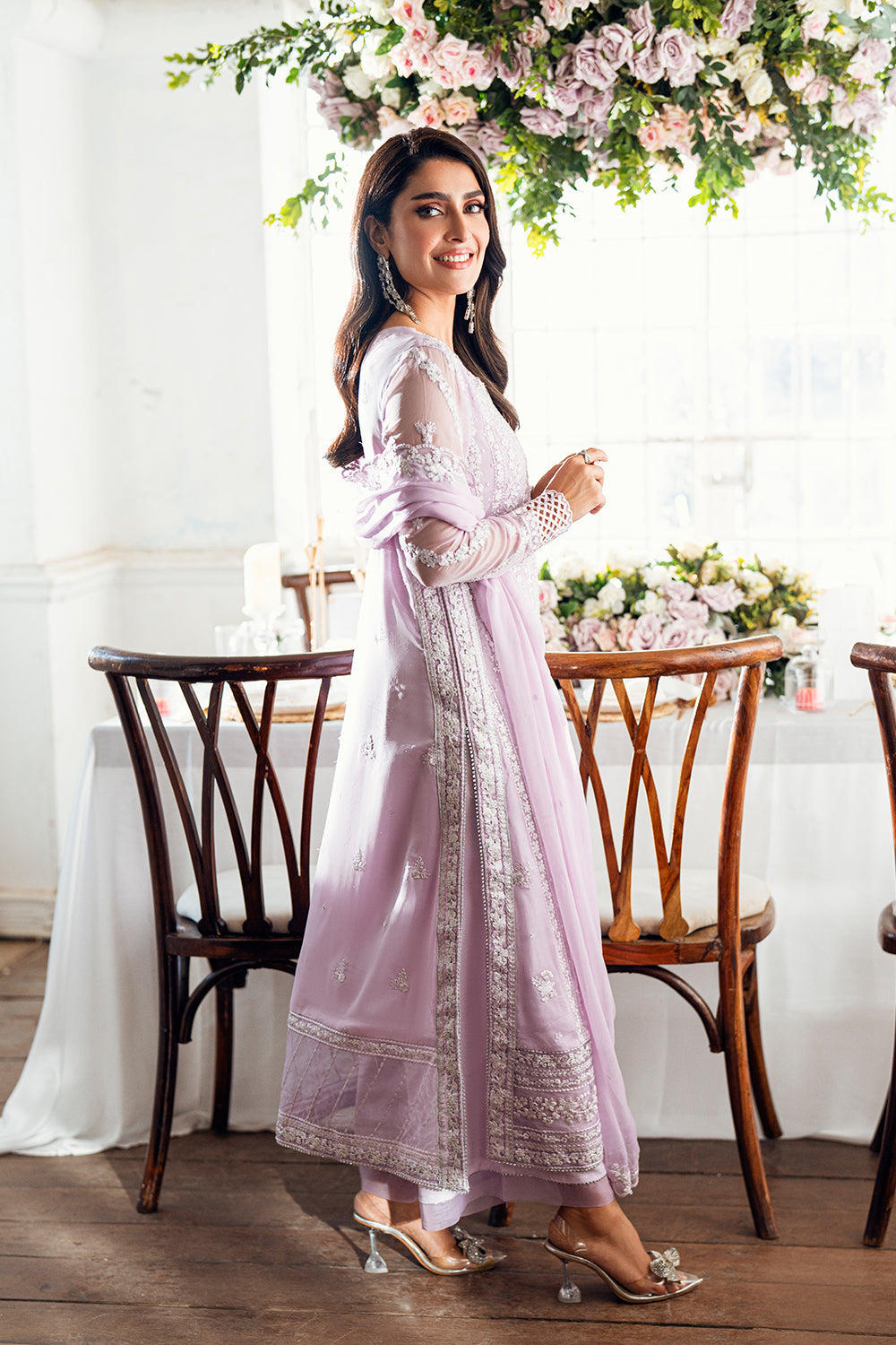Woman in a light pink traditional outfit standing in a decorated room with floral arrangements.