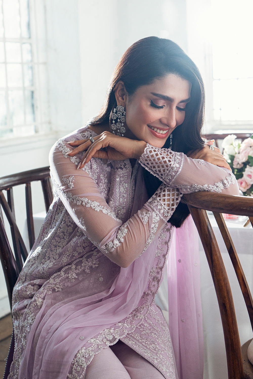 Woman in a pink and silver traditional outfit sitting on a wooden chair with a blurred background