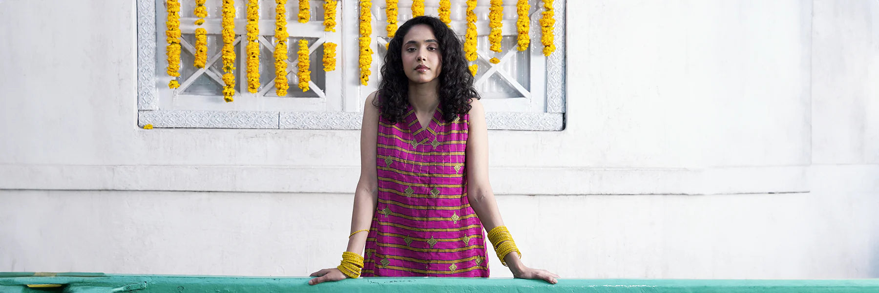 Woman in a pink dress standing behind a green counter with yellow decorations on the wall.